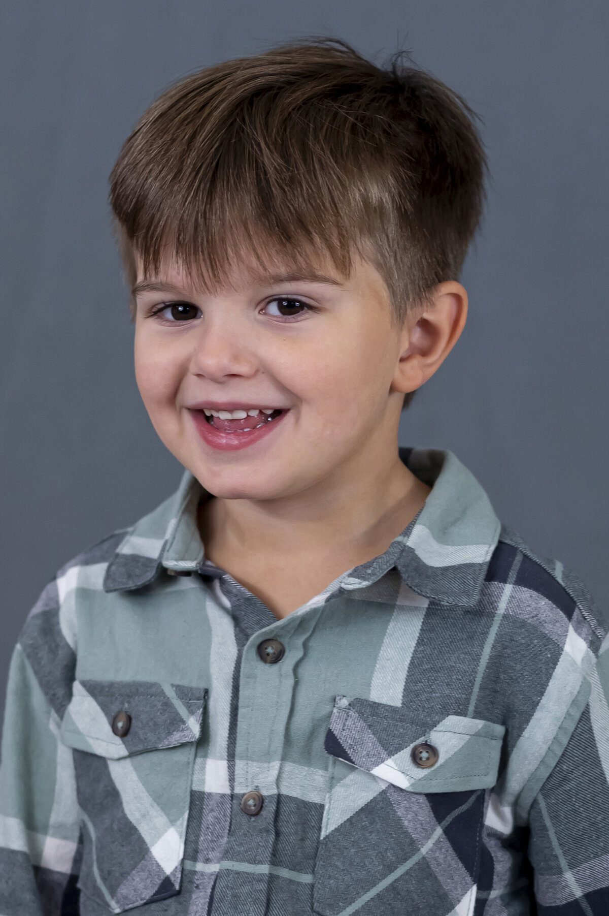 Preschool boy smiling while sitting in front of a grey backdrop for his back to school photos in Vancouver, BC.