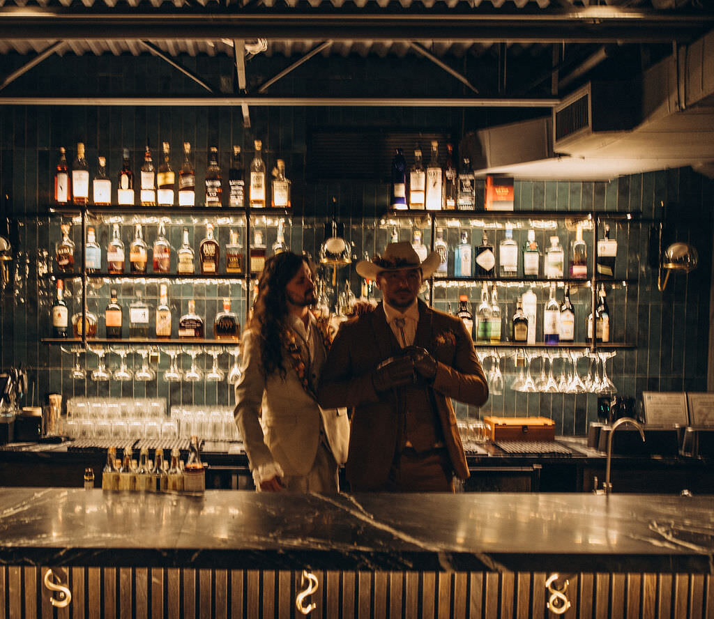 A wedding couple standing behind a bar together.