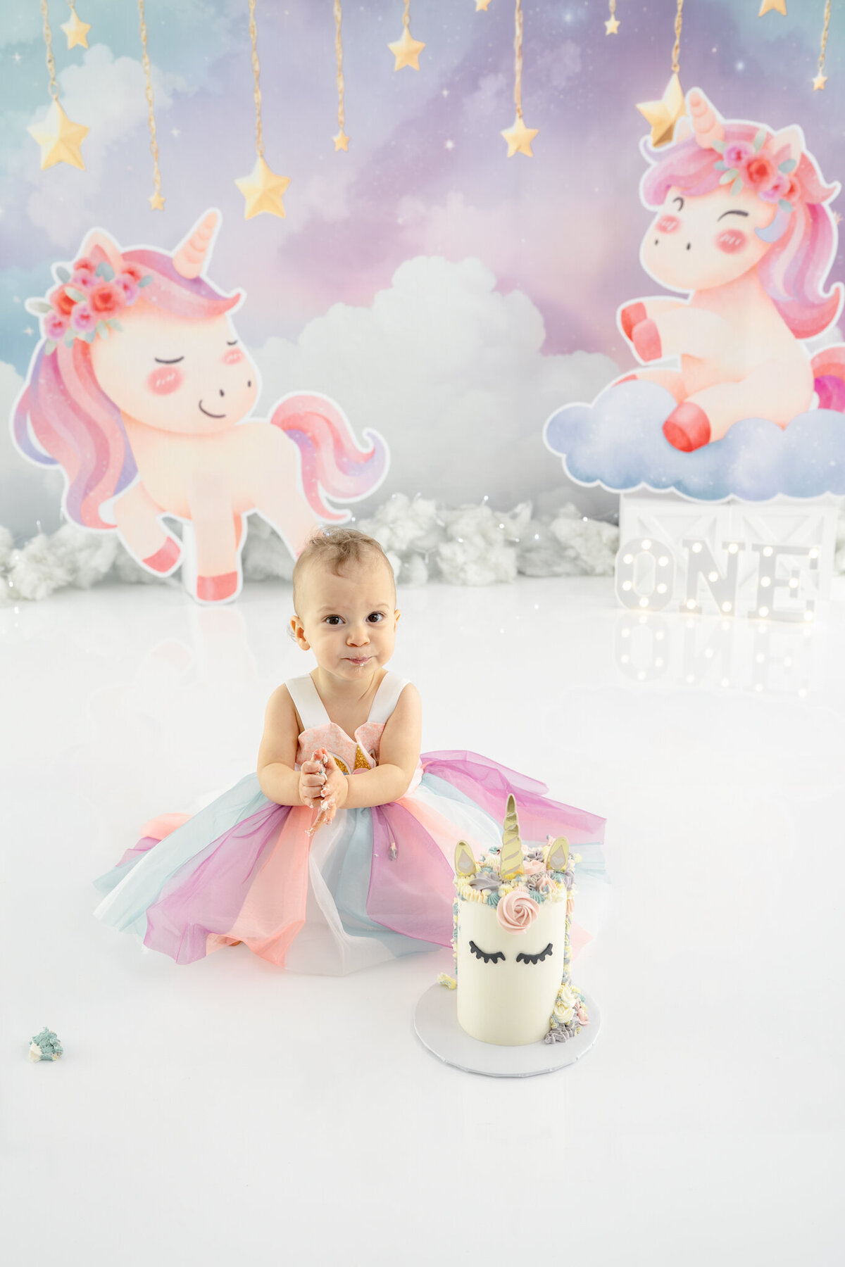 Girl in unicorn dress eating unicorn cake during themed cake smash session— captured by Alliston and Barrie cake smash photographer.