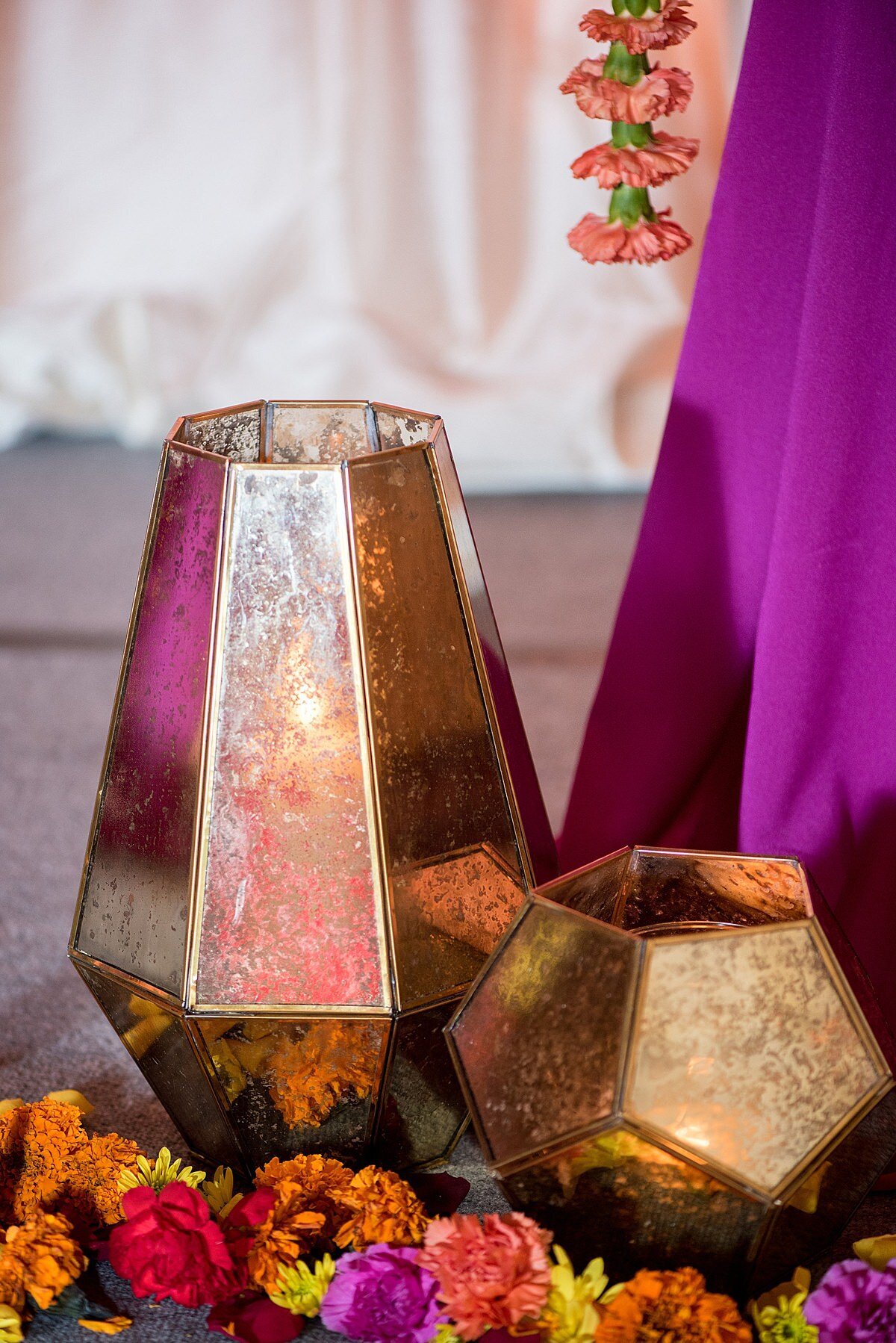 Gold mirrored candle holders surrounded in orange, red, magenta and yellow flowers at the base of a mandap in Nashville, TN at an Indian wedding