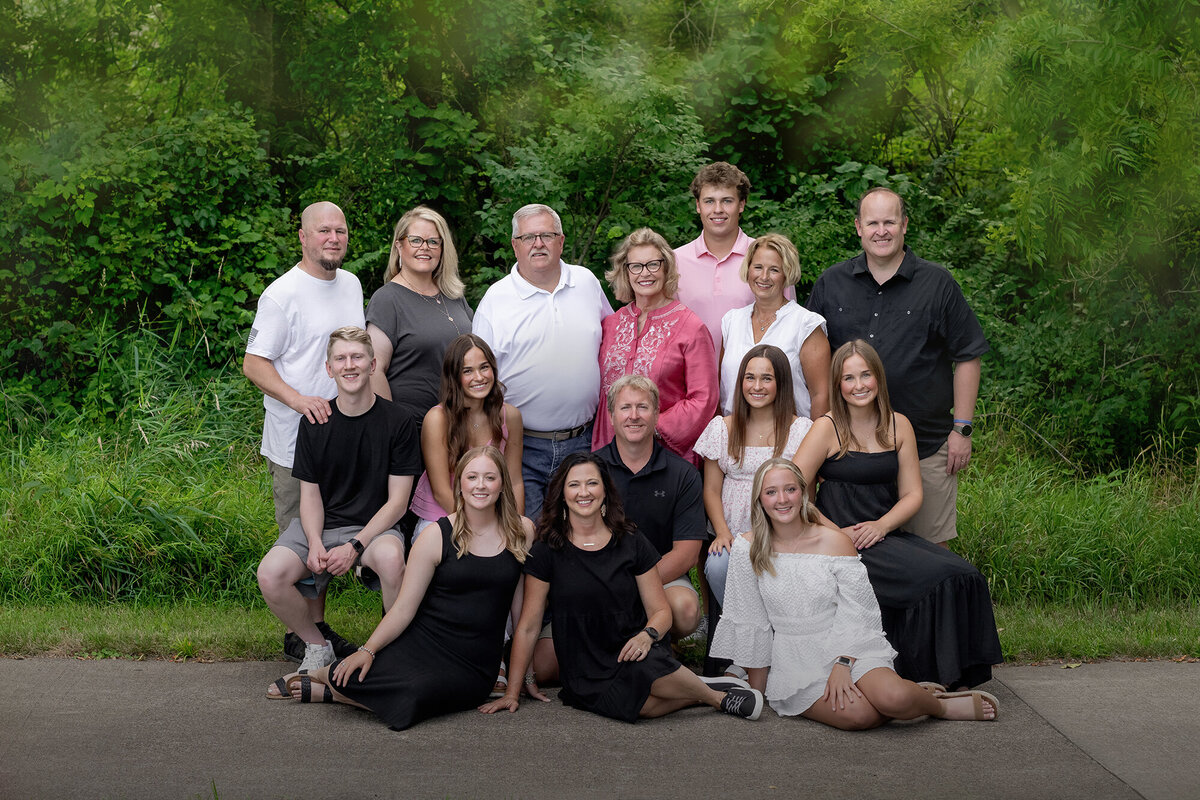 A large family sits and stands in front of a wooded area