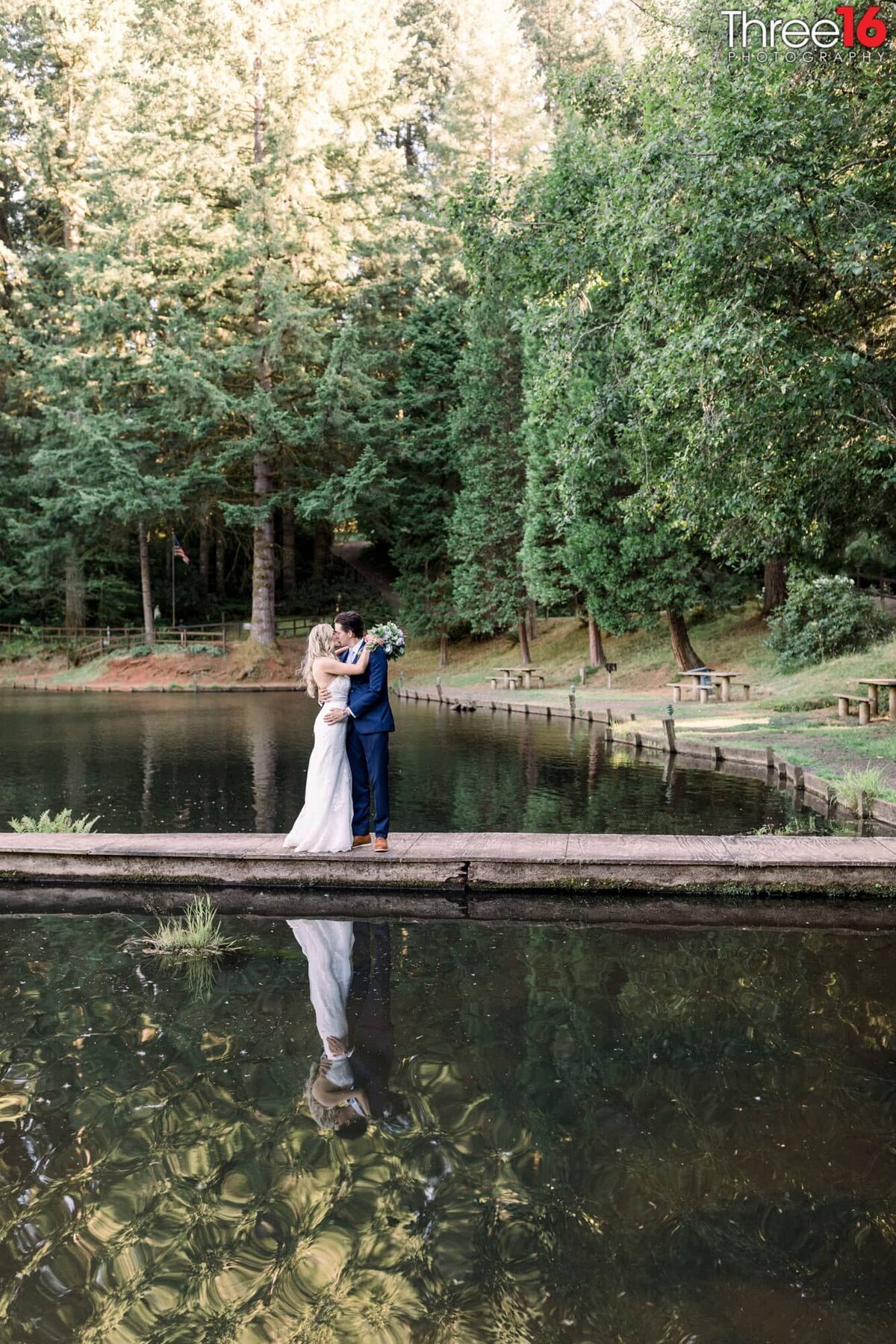 Bride and Groom share a romantic kiss alone on a dock that goes into the lake