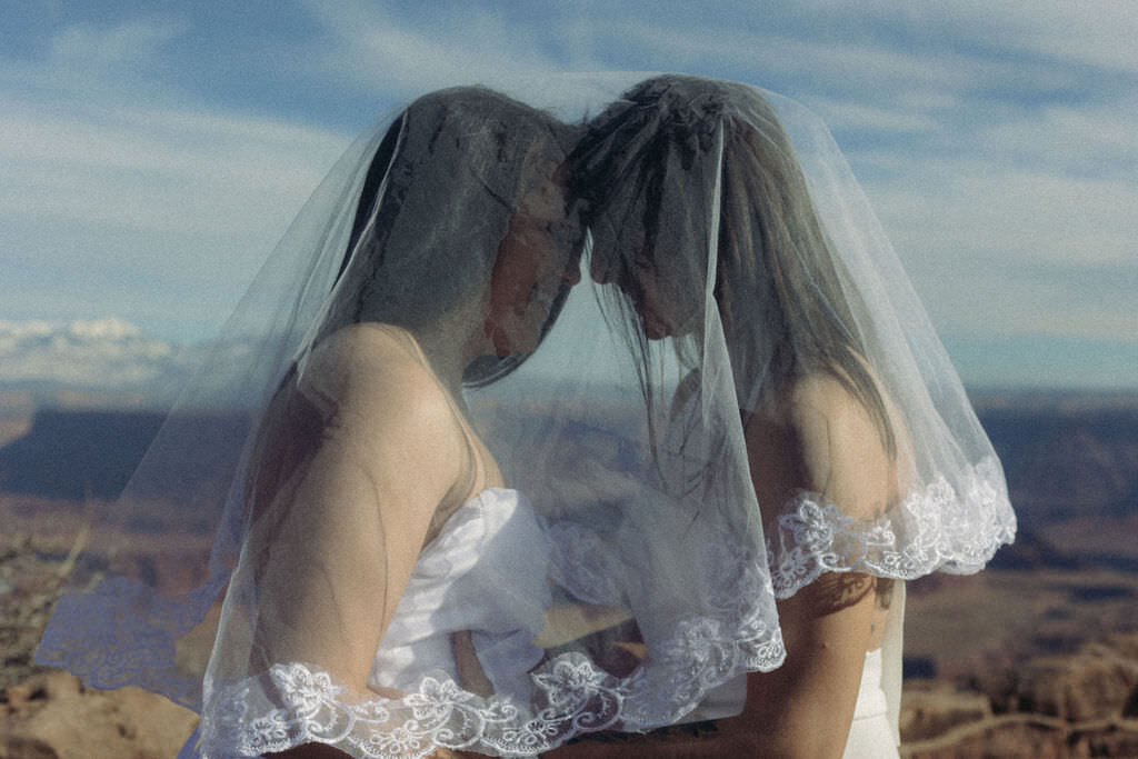 A couple standing forehead to forehead with a veil over them.