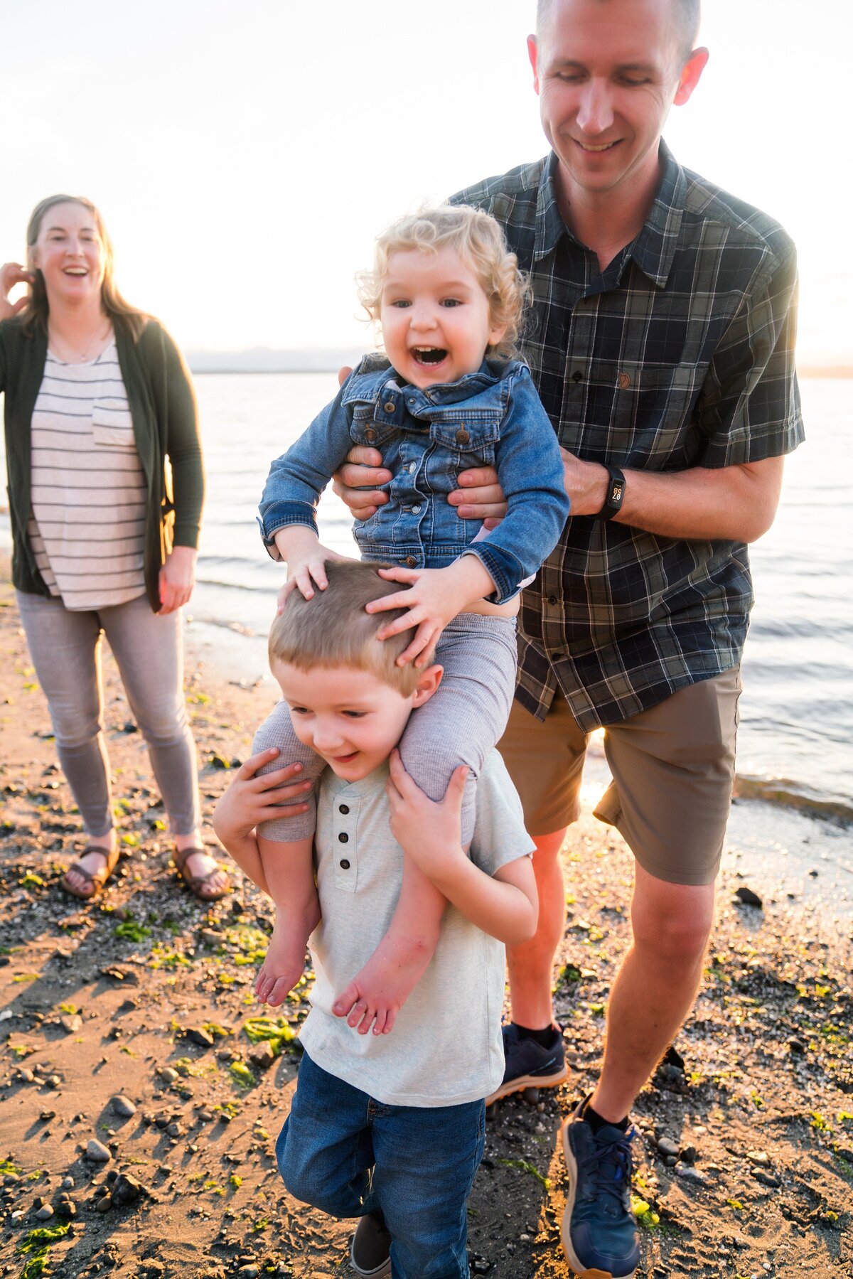 Brother giving sister shoulder ride with dad's help as mom watches in the background at Carkeek Park Beach