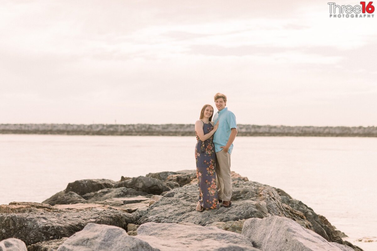 Engaged couple stand together on the Corona del Mar State Beach jetty