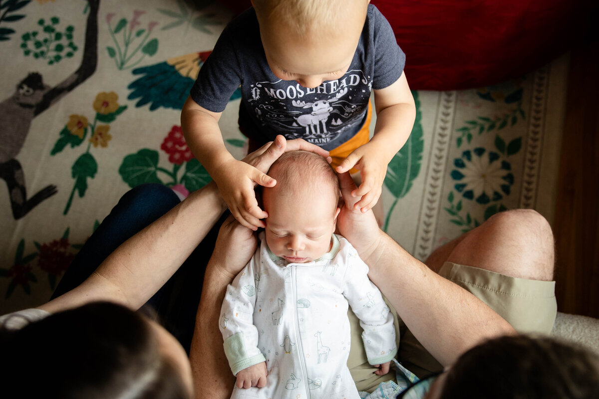 Mom and Dad holding baby with big brother touching baby's face