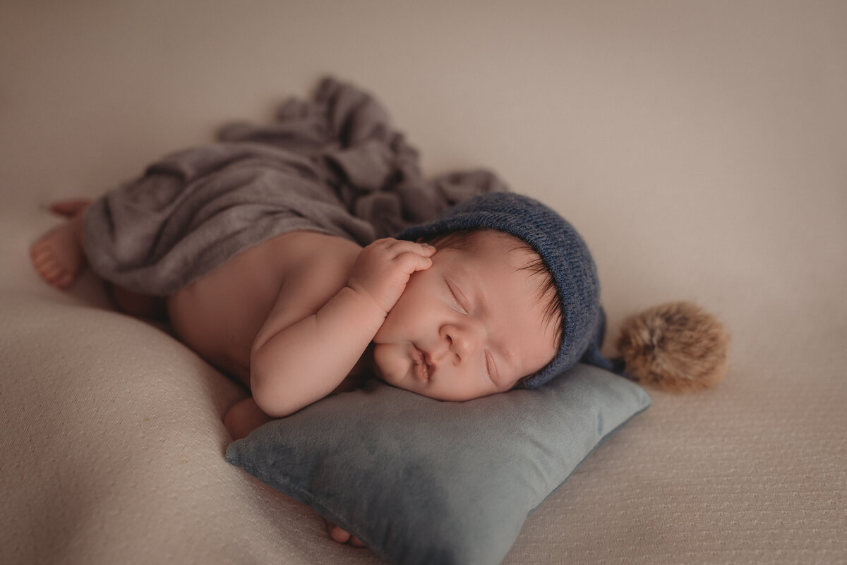 Newborn photo session at Atlanta GA photography studio with baby boy asleep on side wearing blue cap