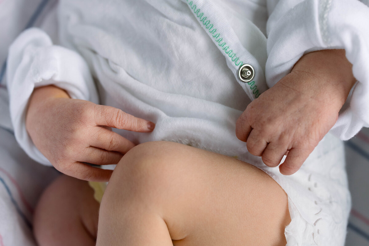 Close up photo of babies hands and leg dressed in hospital shirt