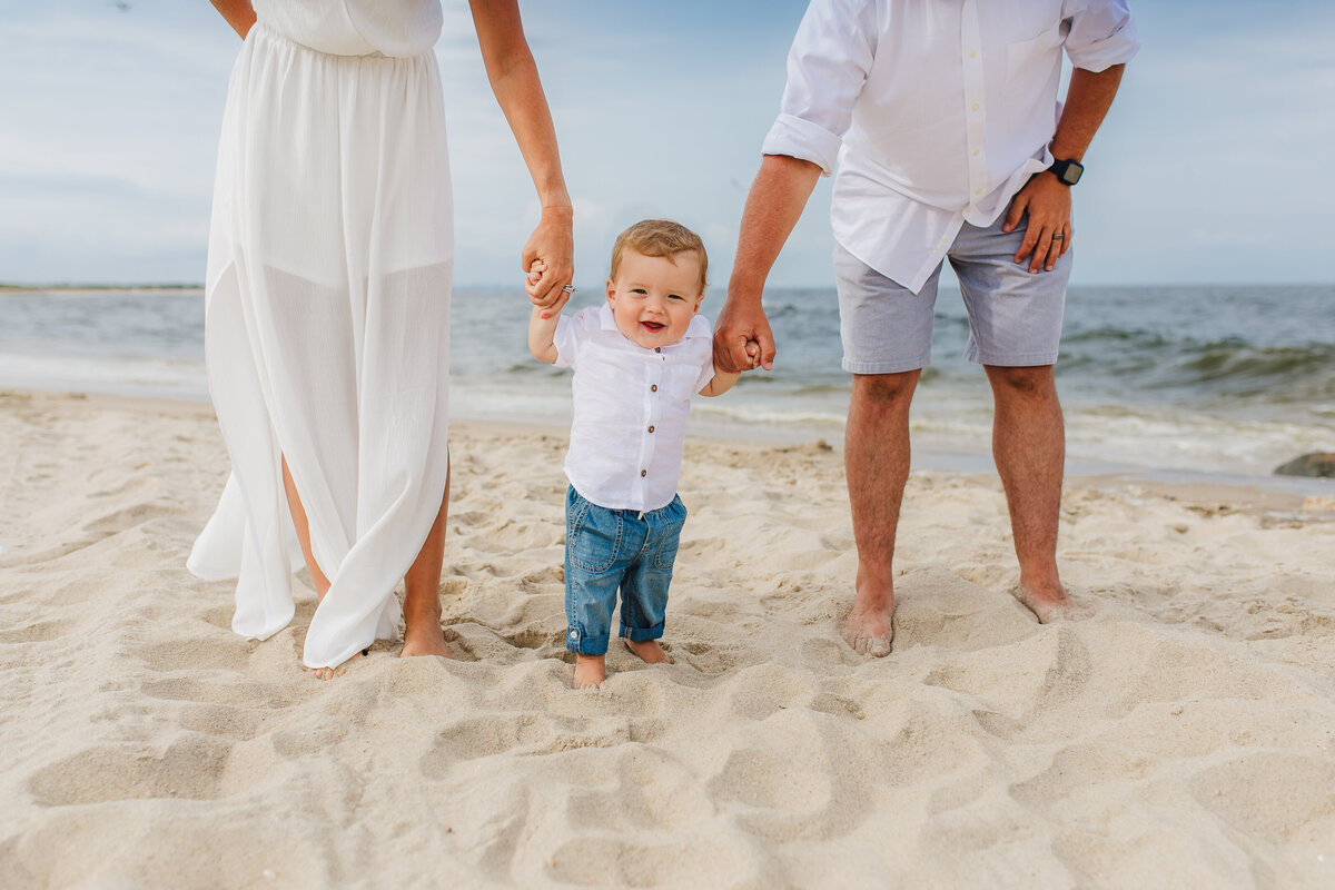 baby boy holding parents hands on beach