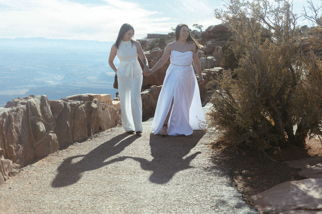 A newlywed couple walking along the edge of a canyon.