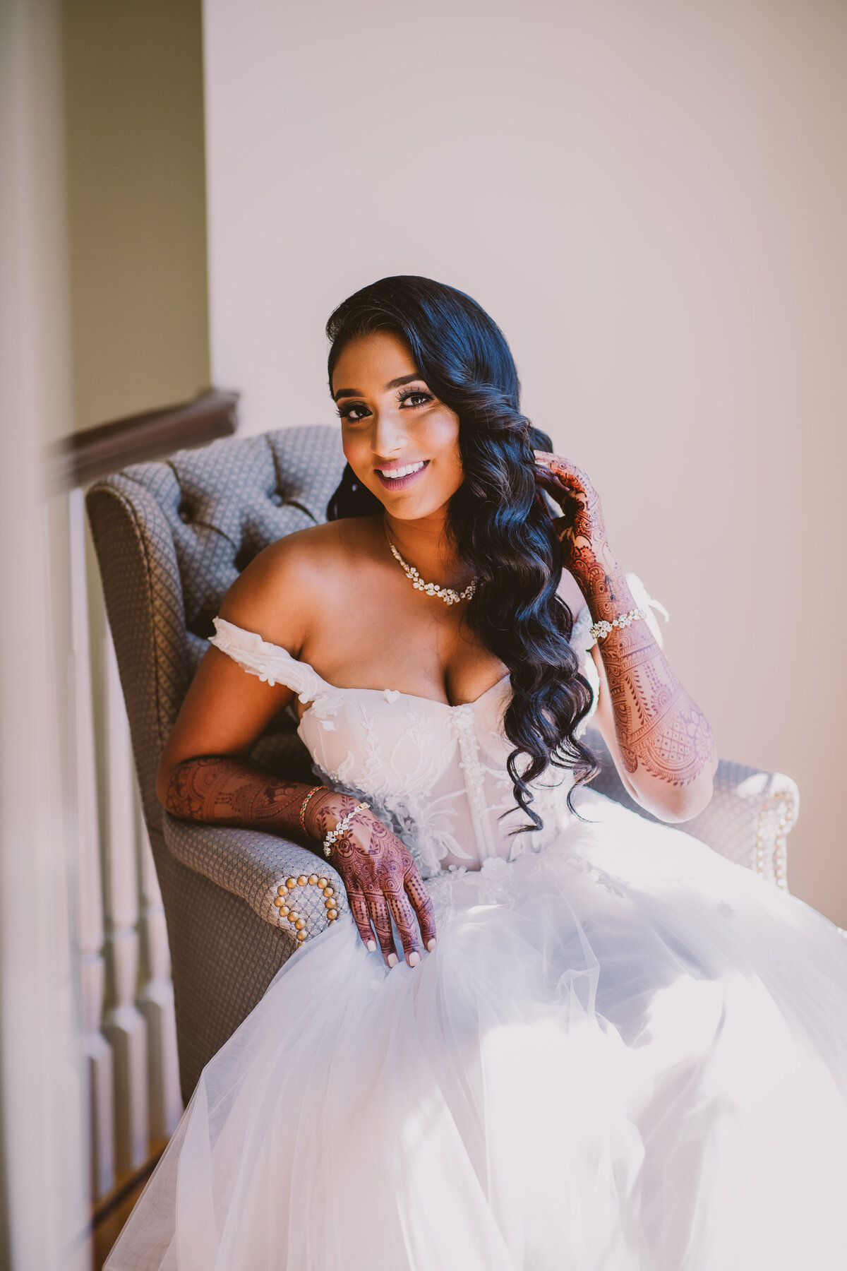 Indian bride sitting on a chair indoors and smiling at the camera on the wedding day