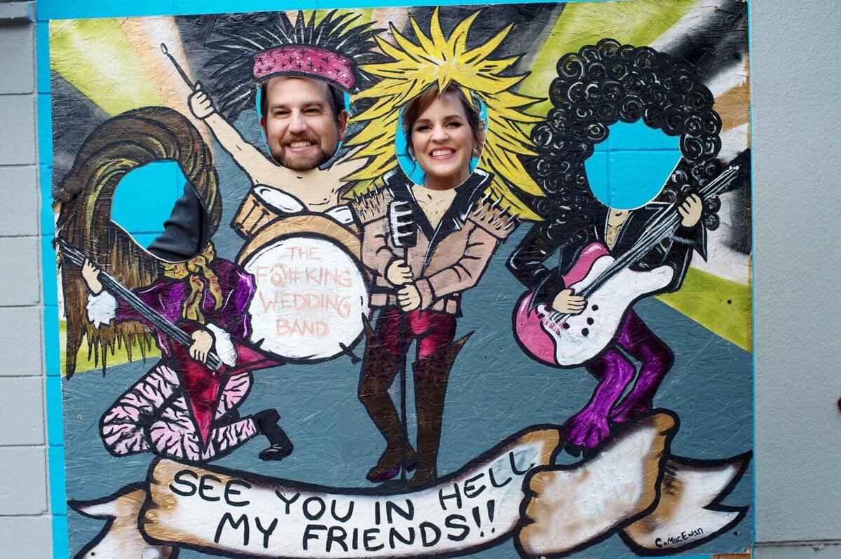 a bride and groom stick their heads through a painting of a rock band