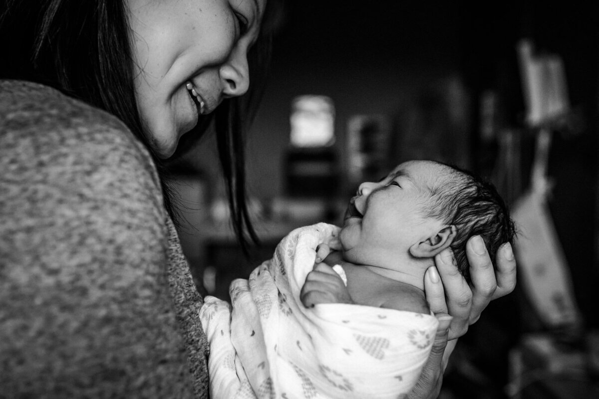 mom and swaddled newborn smiling at each other in the hospital