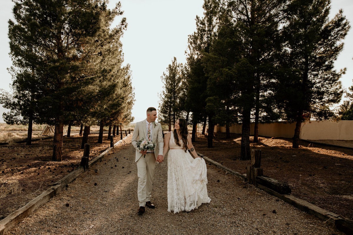 bride and groom walking together through trees in the desert