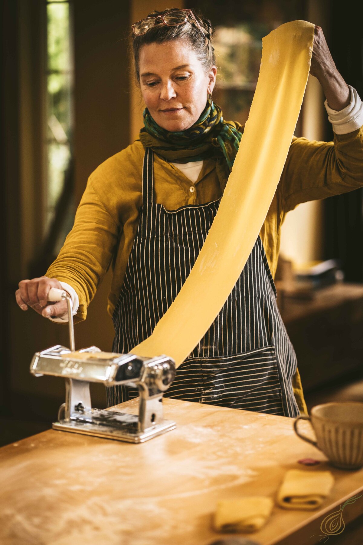 A woman skillfully cuts fresh pasta on a wooden table, showcasing her culinary expertise and attention to detail.