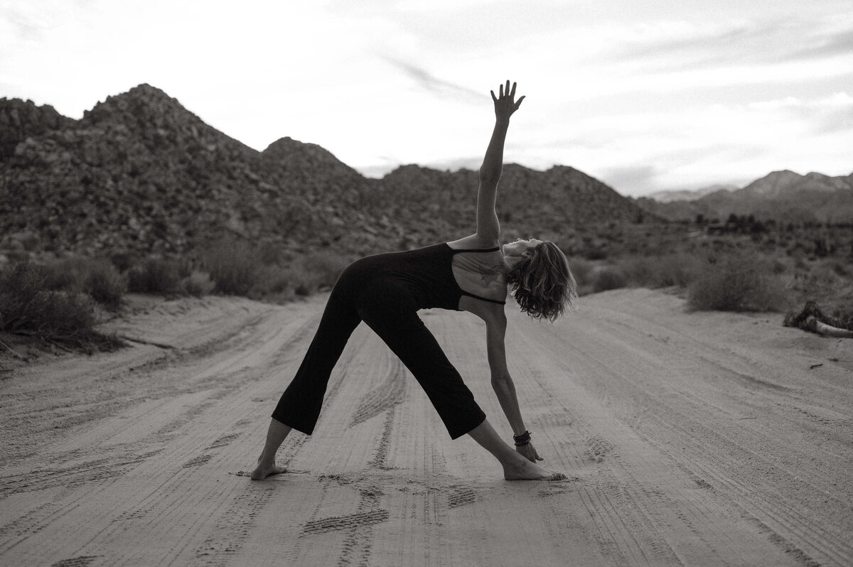 In black and white, a woman performs yoga on a quiet road, finding peace and appreciating the beauty of her environment.