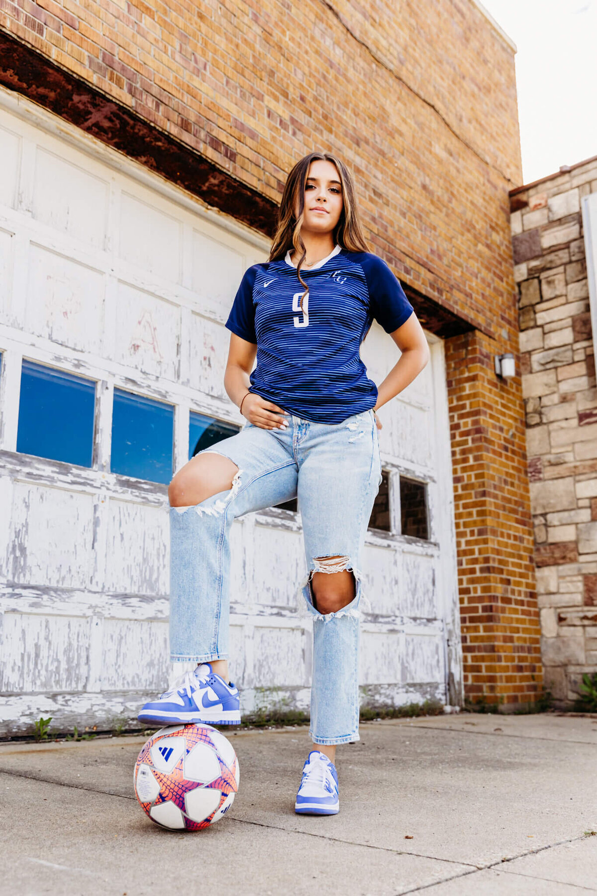 pretty high school girl standing with her foot on her soccer ball and looking fierce for her senior photography session