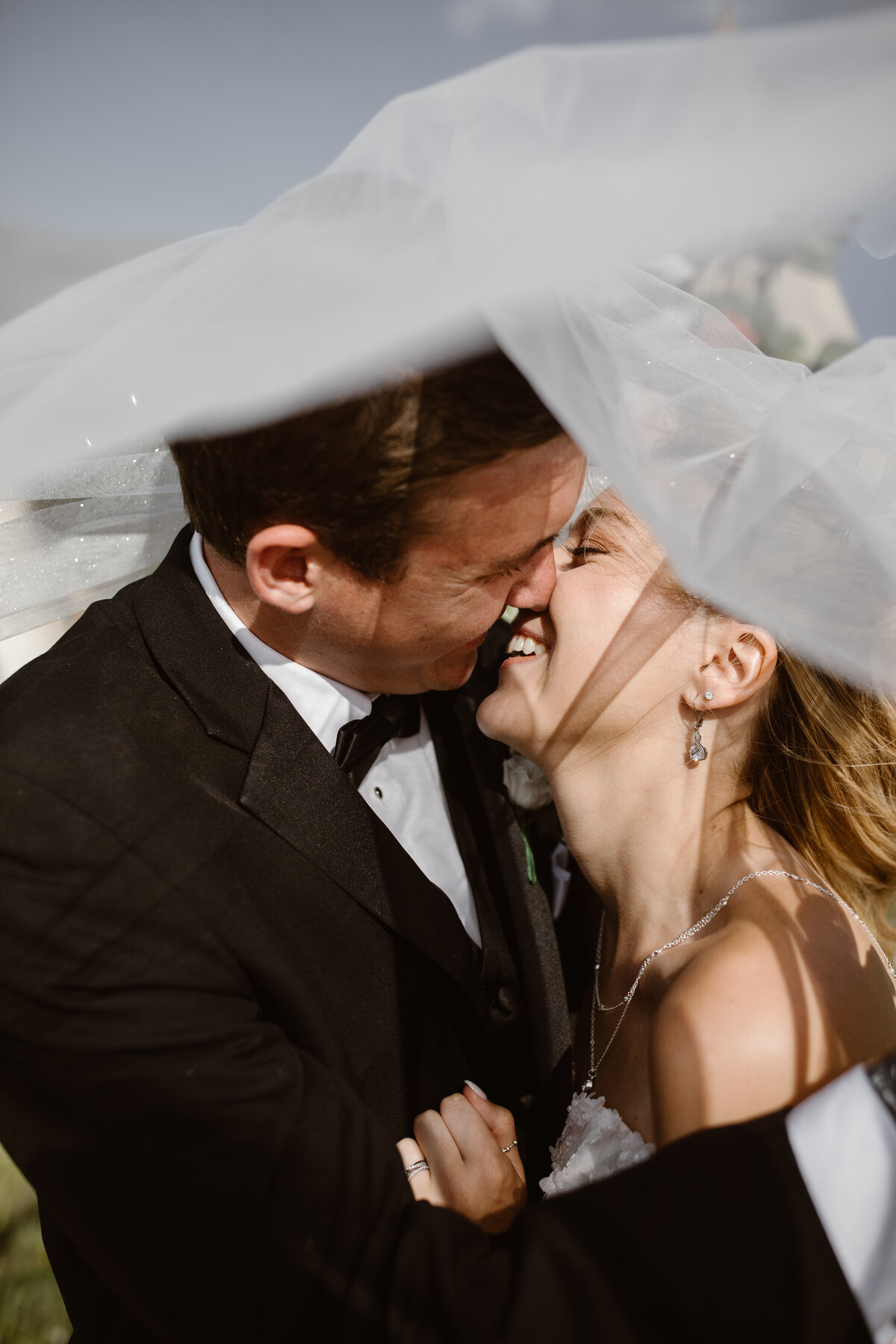 Bride and groom laugh and lean in for a kiss under the bride’s flowing veil during their wedding in Breckenridge, Colorado.