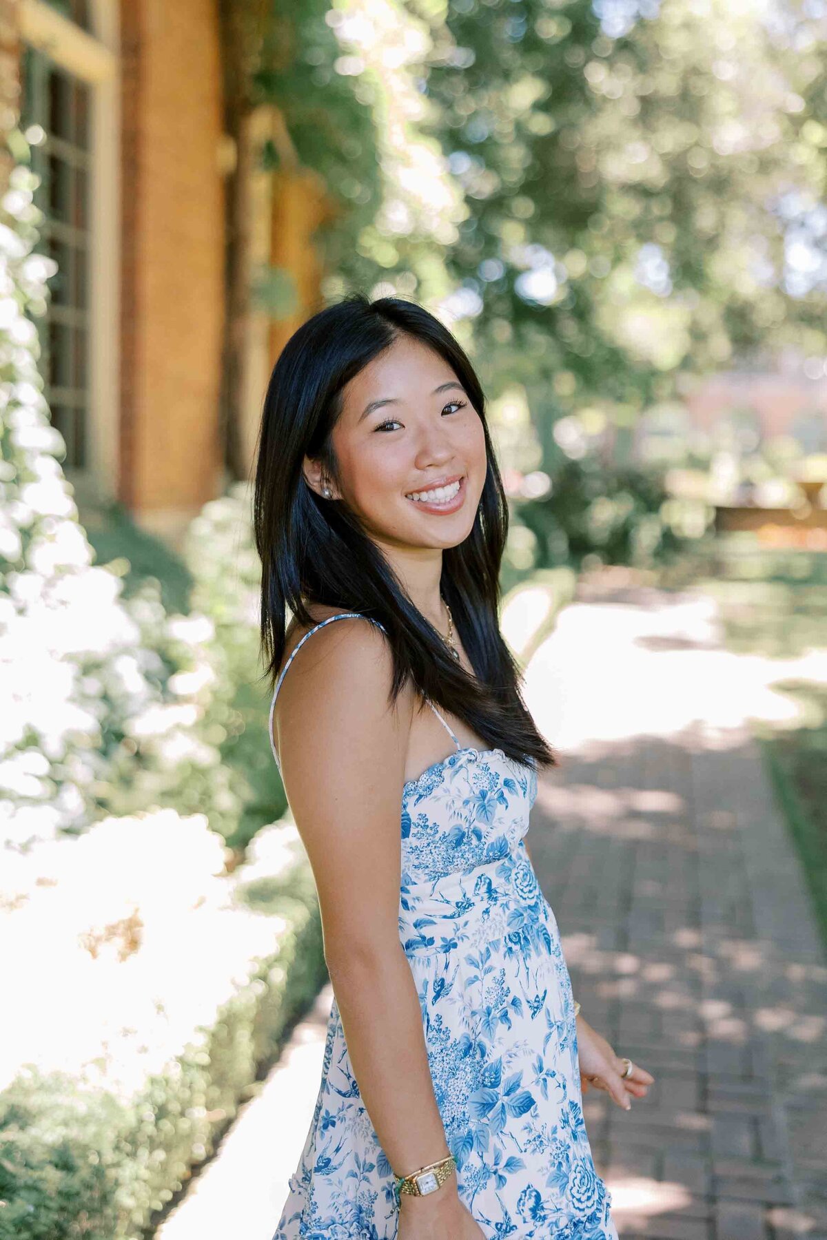 Asian girl with long black hair smiling over her shoulder and wearing a white and blue floral dress with spaghetti straps