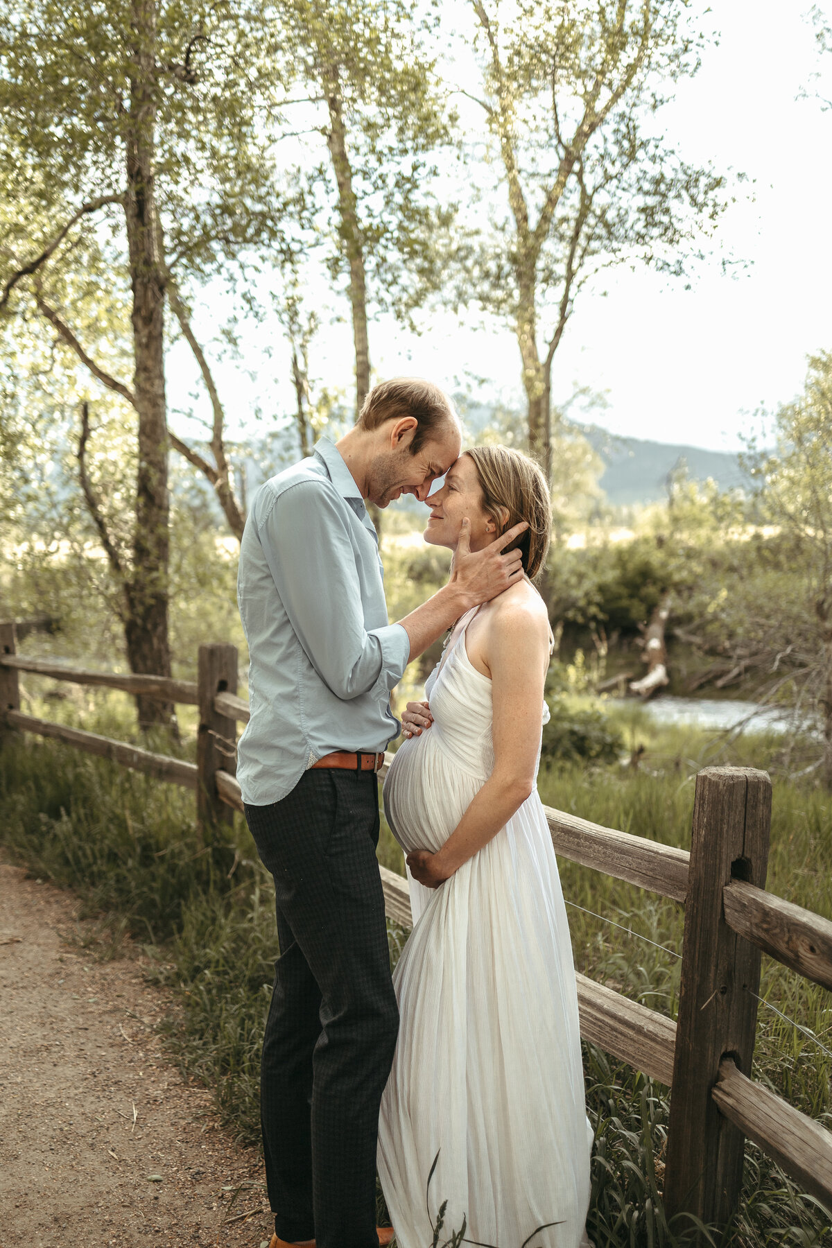 expectant parents standing in front of fence looking at each other closely during maternity session in firestone colorado with alexis adkins photography