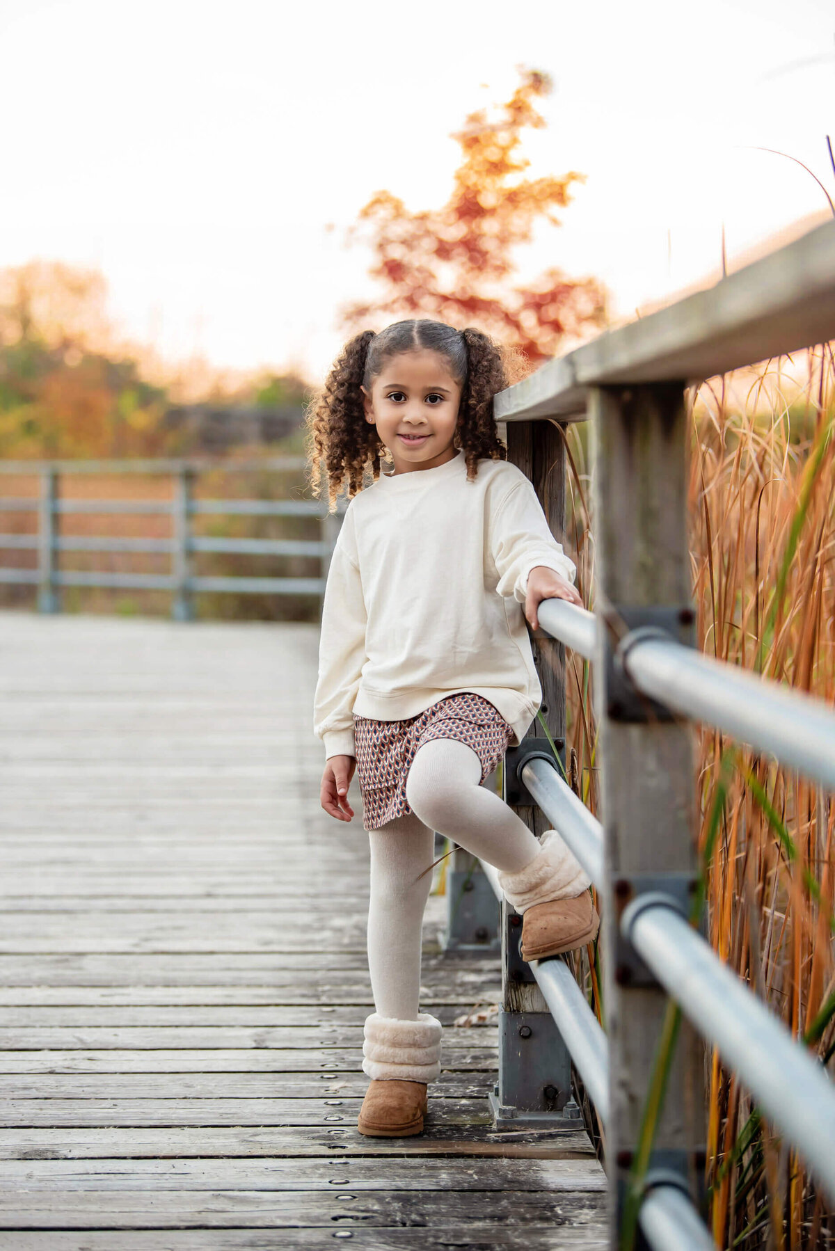 Little girl with her foot up on a bar on a bridge for her fall family photography session in Burlington, ON