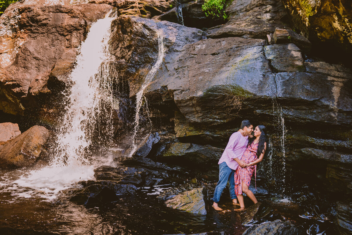 A couple sharing a moment during their engagement session under a waterfall at the devils hopyard park in connecticut