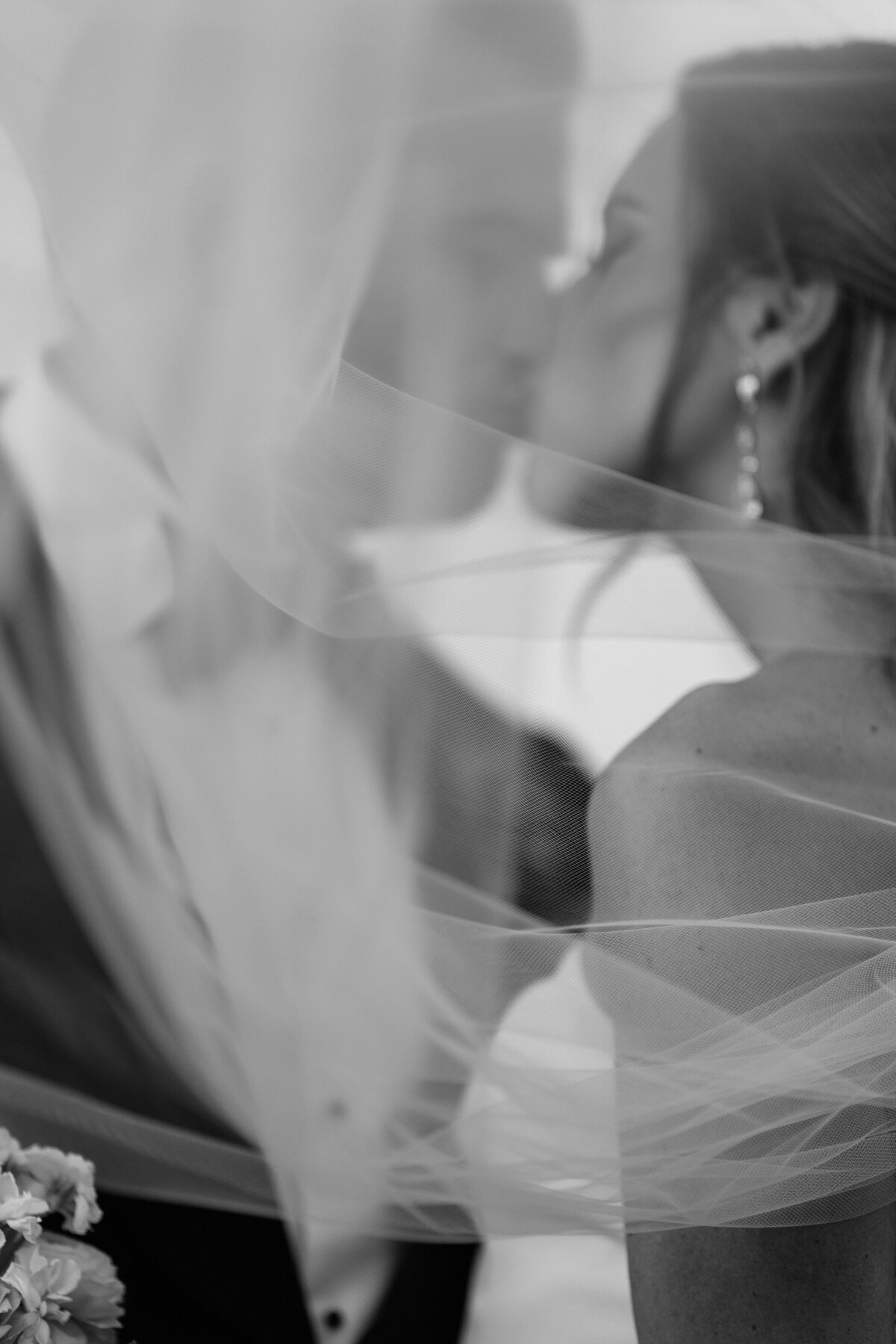Bride and groom kiss while the veil blows around them 