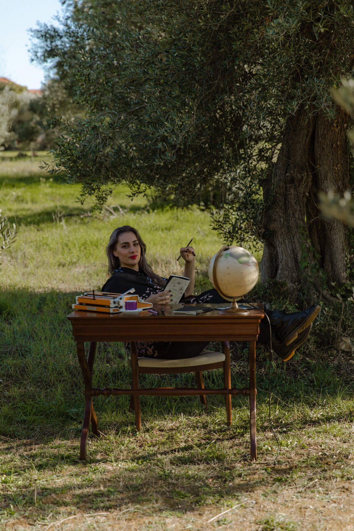 Brand designer working at outdoor desk beneath olive tree in natural office setting