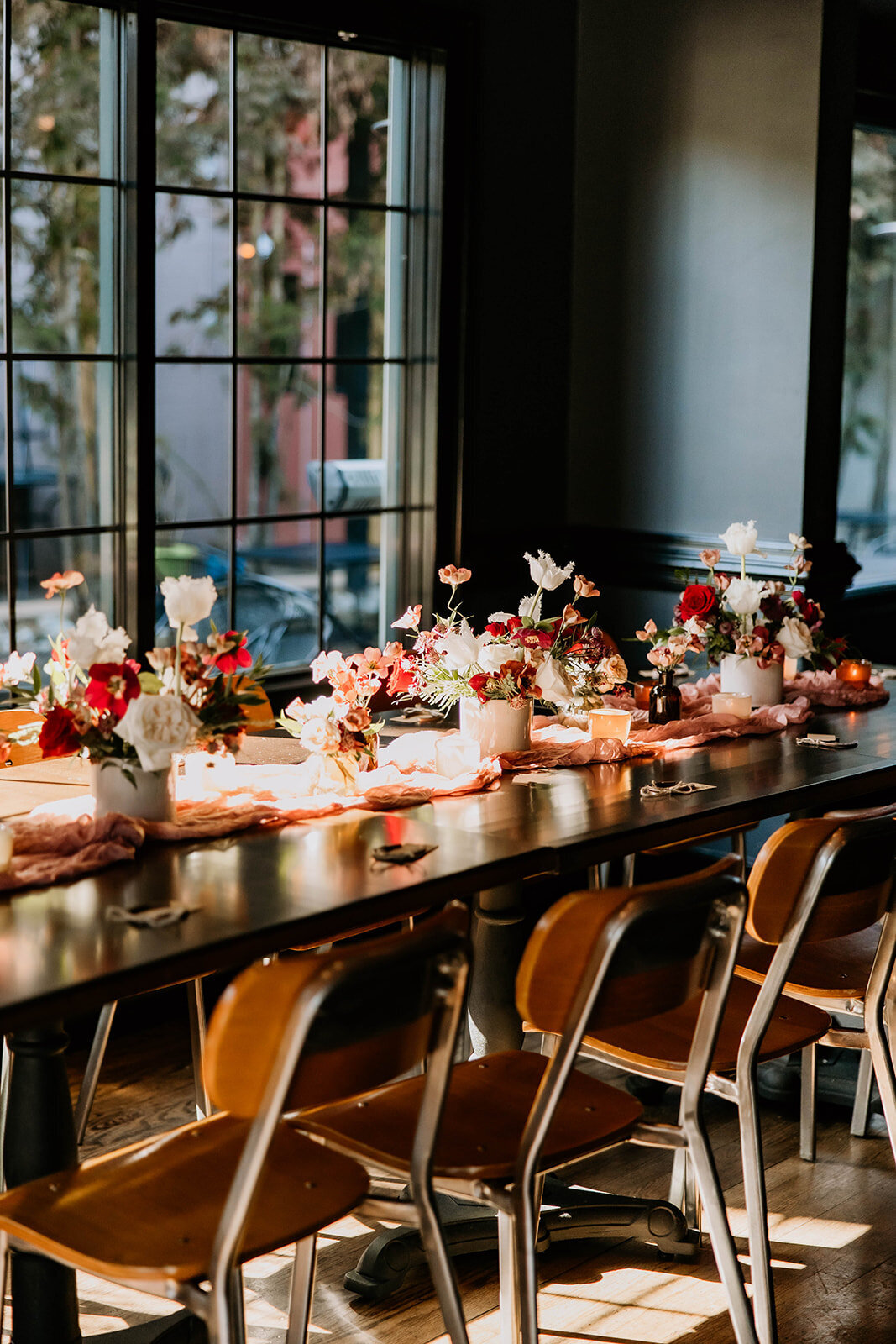 Long wooden table with bold floral arrangements at a brunch celebration in Essex County, NJ.