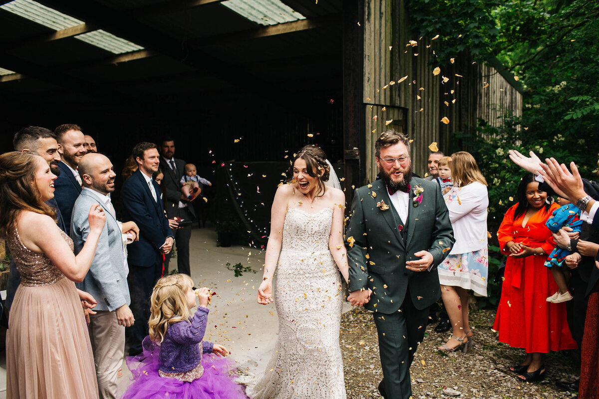 Bride and groom in bottle green suit exiting their humanist wedding ceremony to confetti