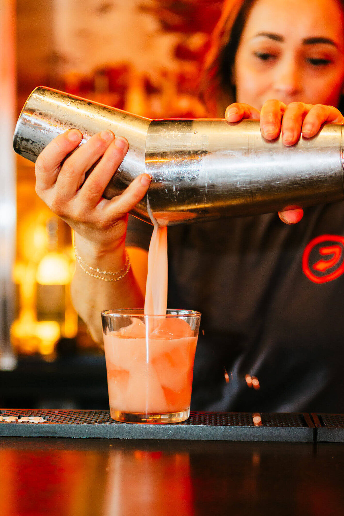 bartender pouring a peach colored cocktail into a cocktail glass