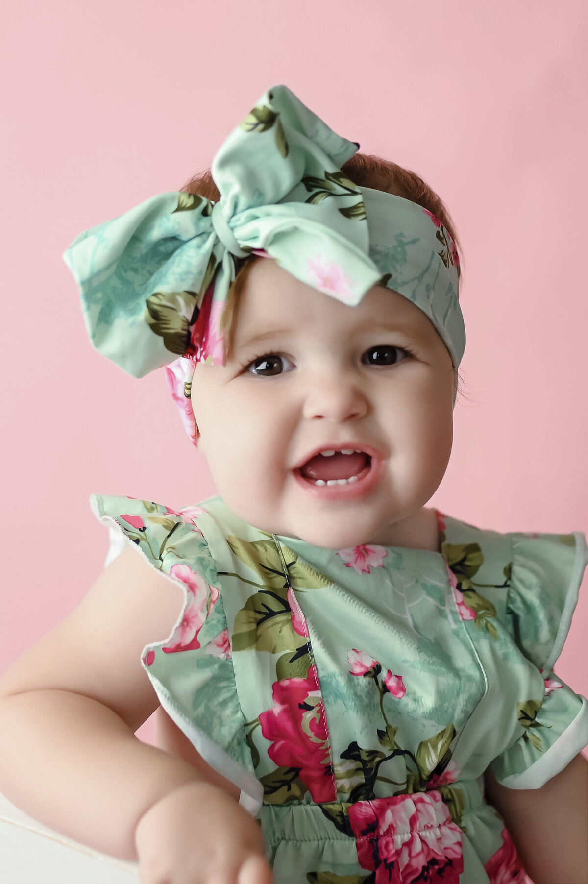 Baby wearing a floral jumper and headband sits in a chair and looks at her Iowa Milestone Photographer