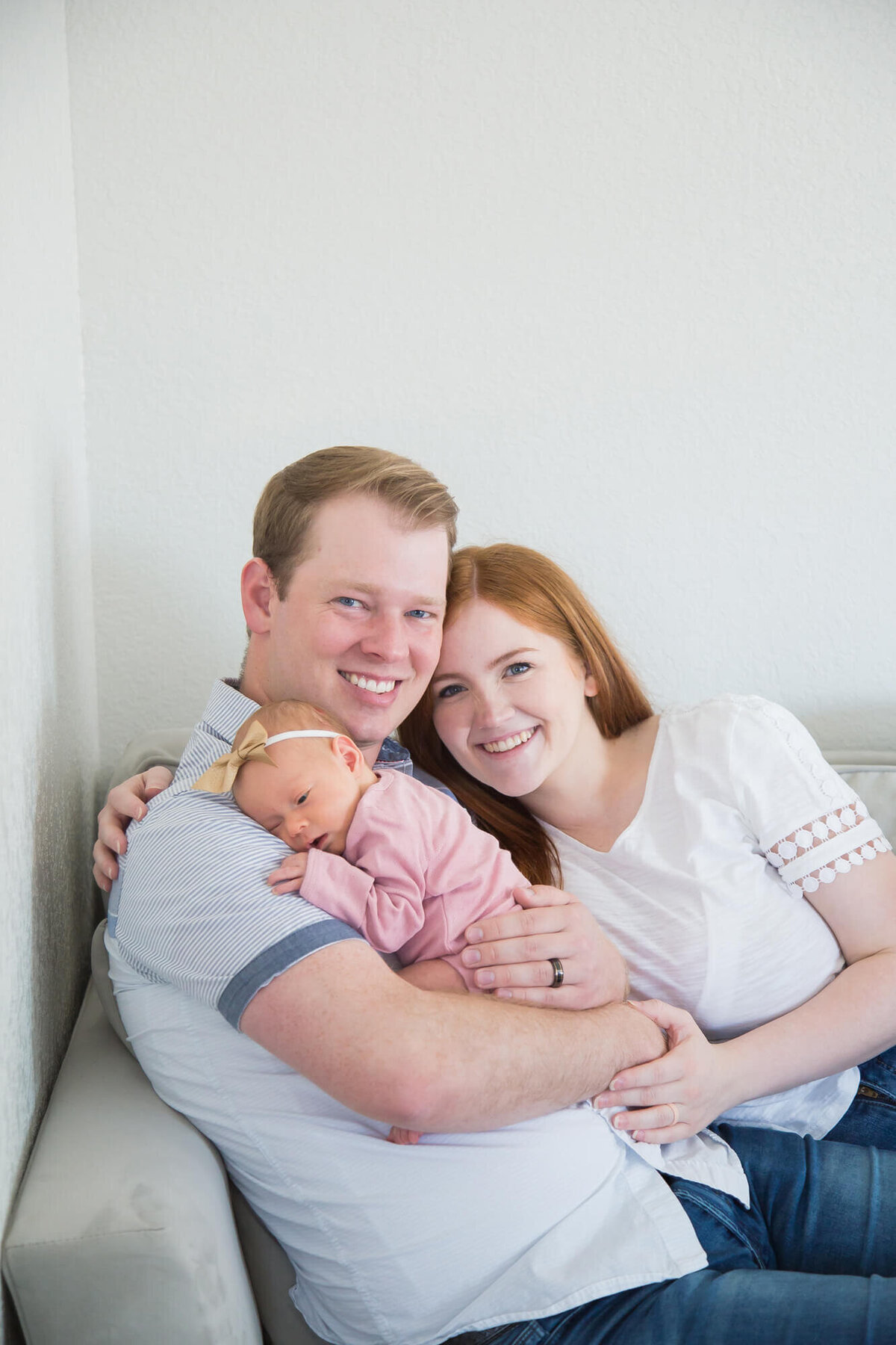 Newborn baby girl snuggled with her parents on a gray couch during newborn photos