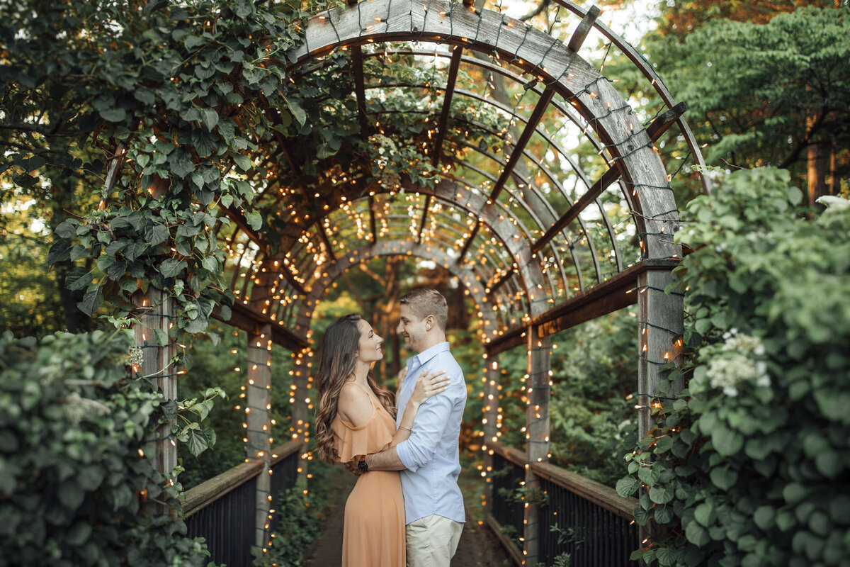 Couple under string lights during summer engagement photo at Sayen House and Gardens in Hamilton Township New Jersey