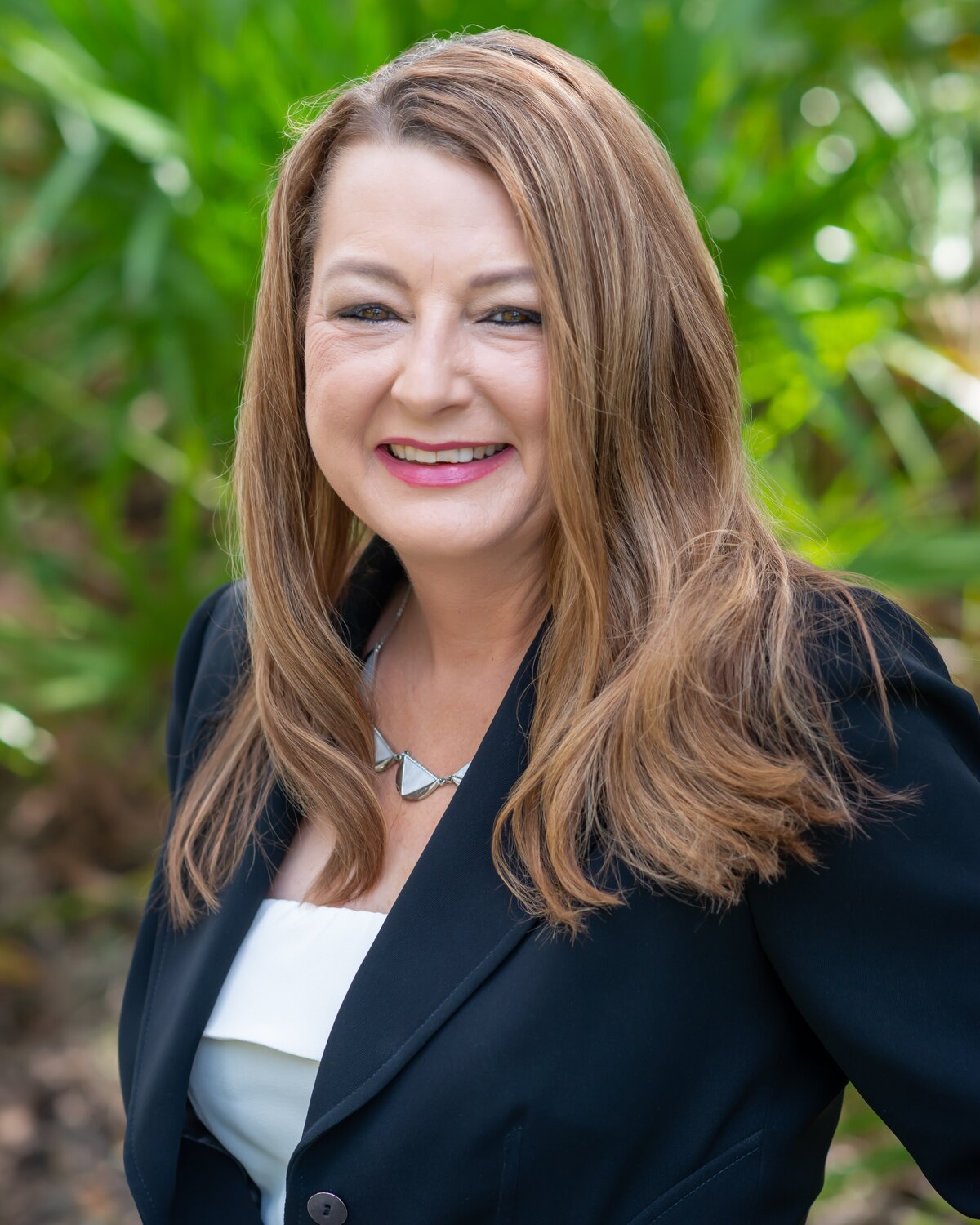 A realtor is posing in front of greenery for her outdoor headshot session.