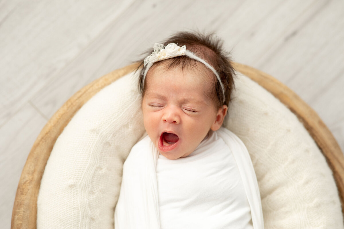 during a Bucks County newborn session a newborn baby girl yawns while swaddled and laying in a basket.