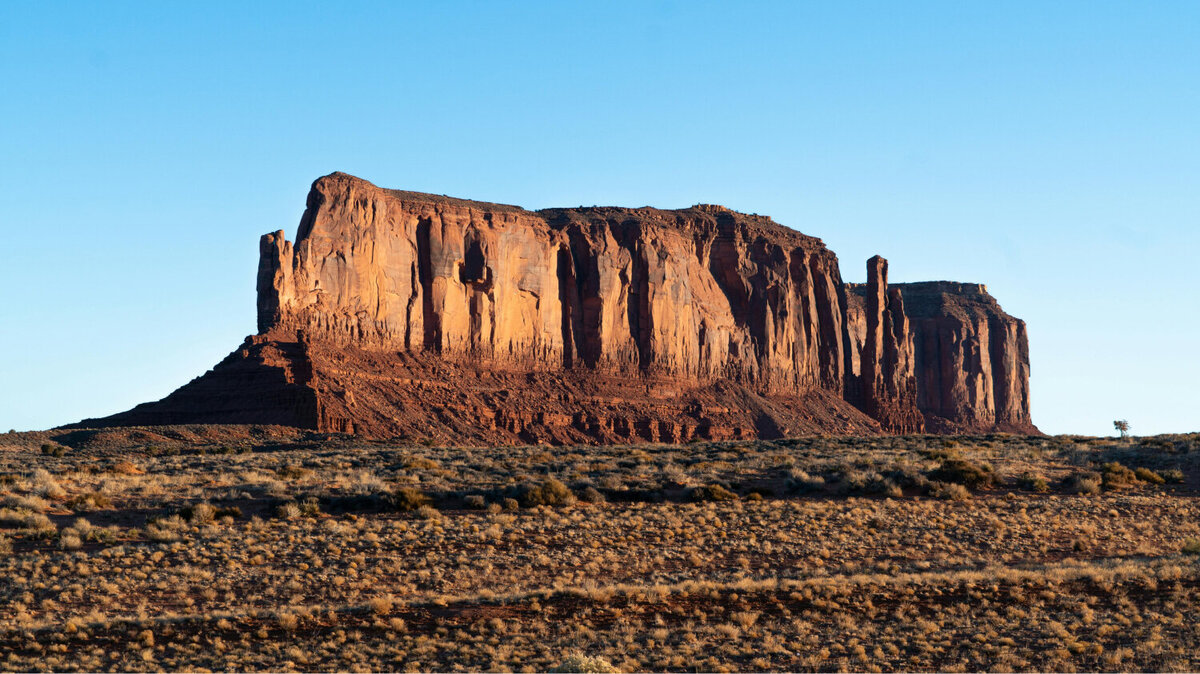 A landscape picture of a large, rocky butte. Around it is blue sky.