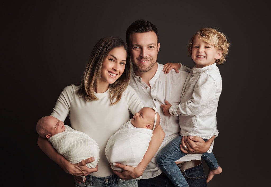 Family of mom and dad, toddler boy and newborn twins of boy and girl smiling at the camera at their Greater Toronto Newborn studio session.