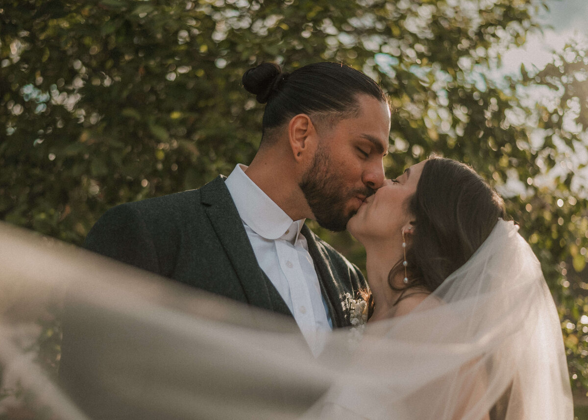 bride and groom kissing with wedding veil in foreground