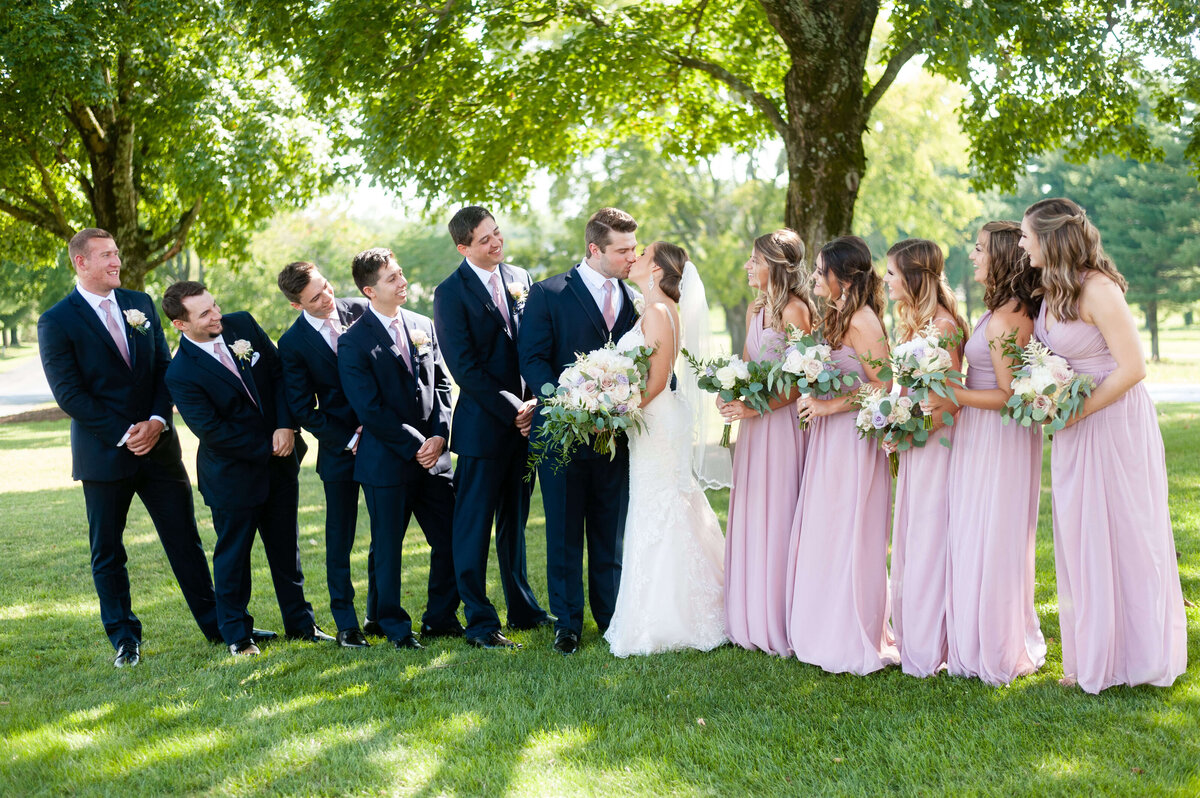 Bride and groom kissing surrounded by bridal party at wedding at Stones River Country Club