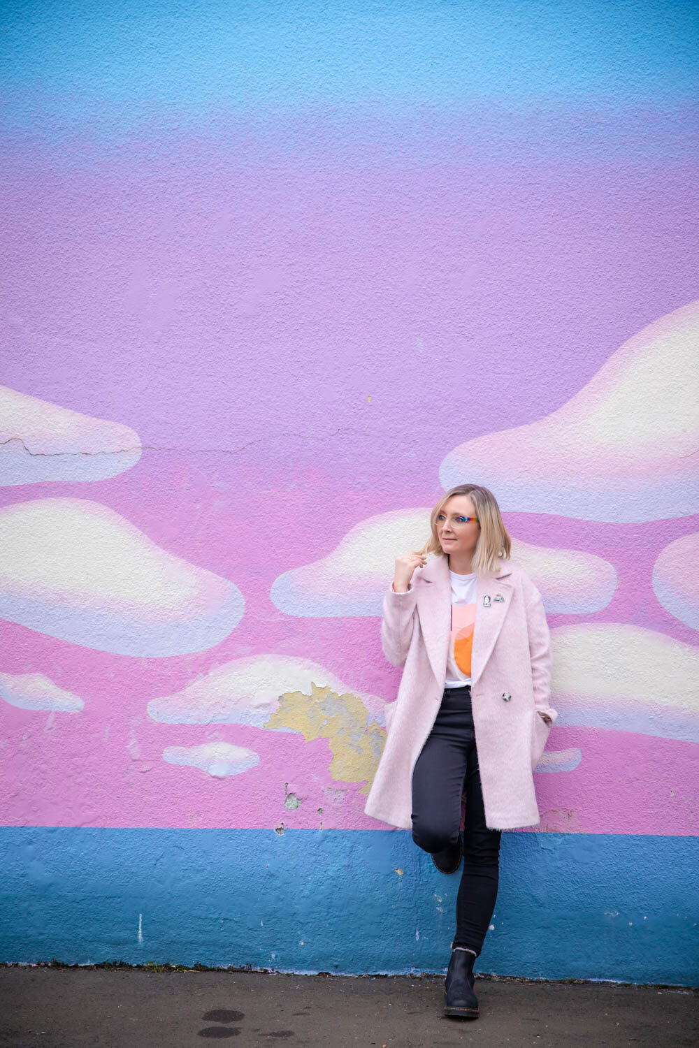 crystal genes photography stands in front of a colorful cloud mural in kenton portland