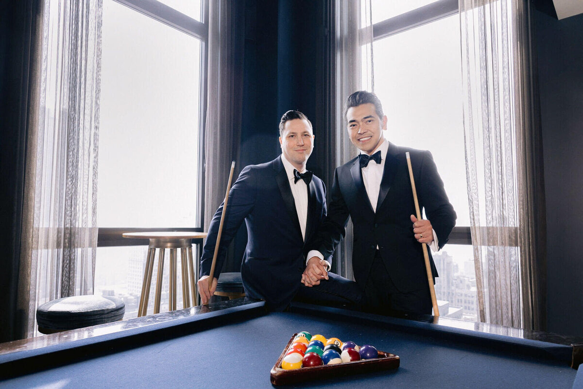 Two grooms are in a room with a billiard table in The Skylark, New York. Wedding Image by Jenny Fu Studio