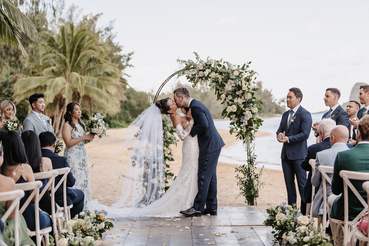 Wedding couple married under a floral covered arch in front of the beach and palm trees