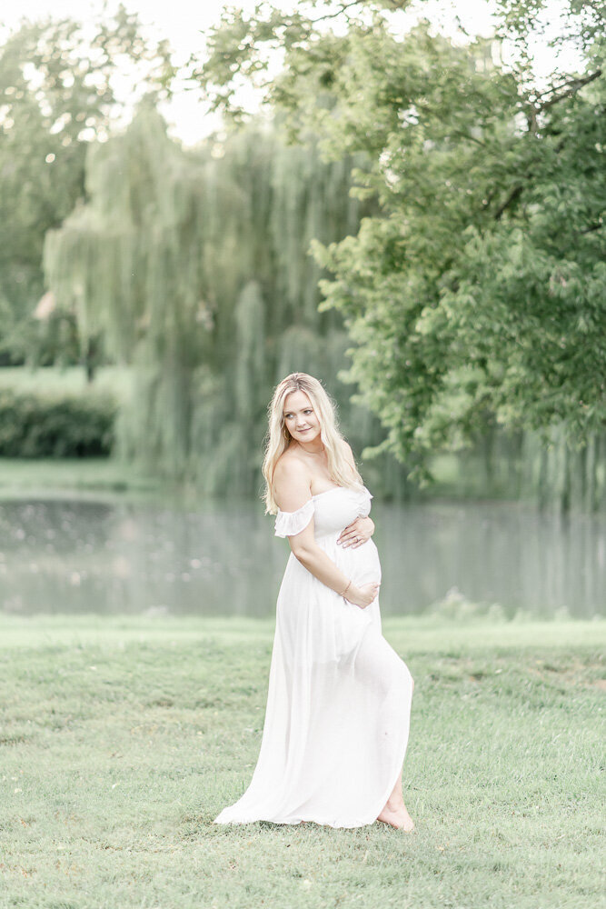 Pregnant woman stands in front of a pond and weeping willow tree By Nashville maternity photographer Kristie Lloyd