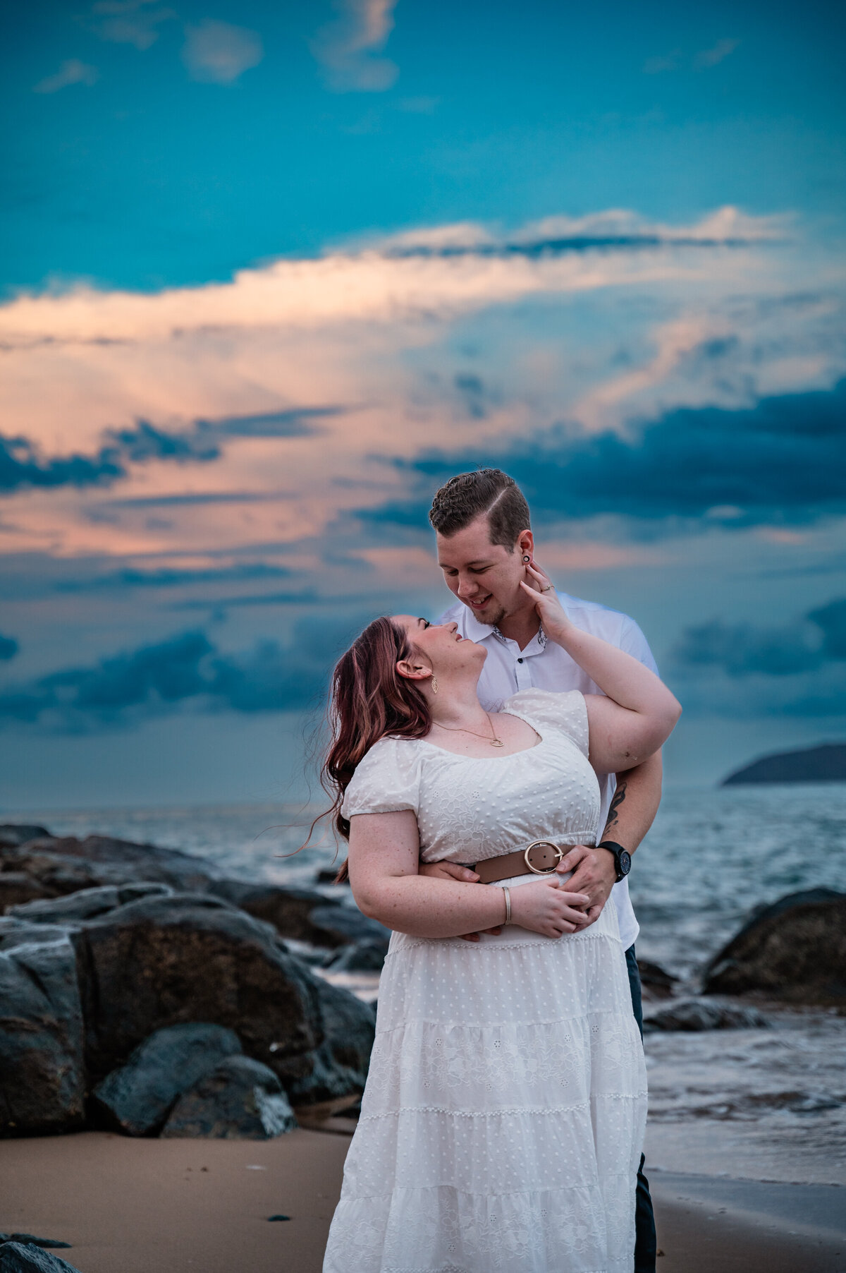 man holding woman as they look at each other with love  while on the beach at sunset - Townsville Engagement Photography by Jamie Simmons