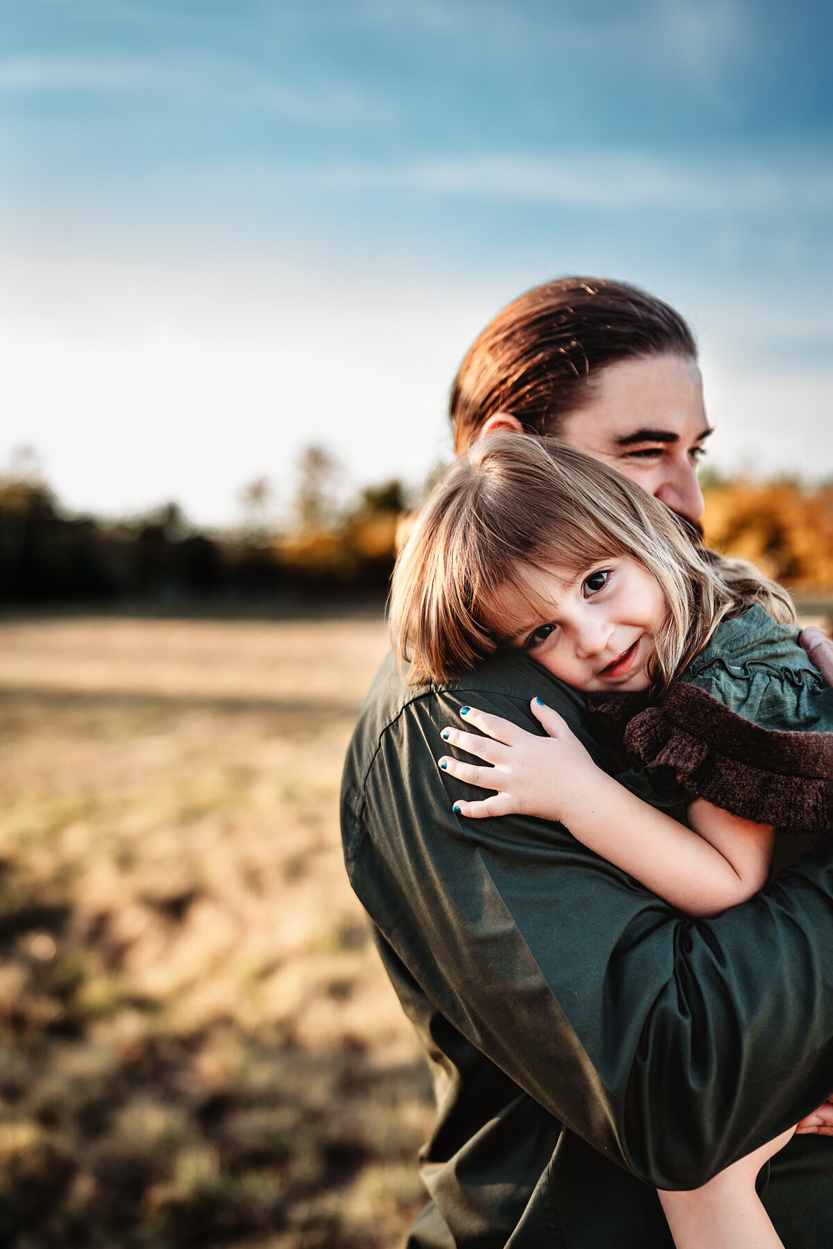 A dad holds his little girl during an outdoor famiy photo session in a San Diego field. 