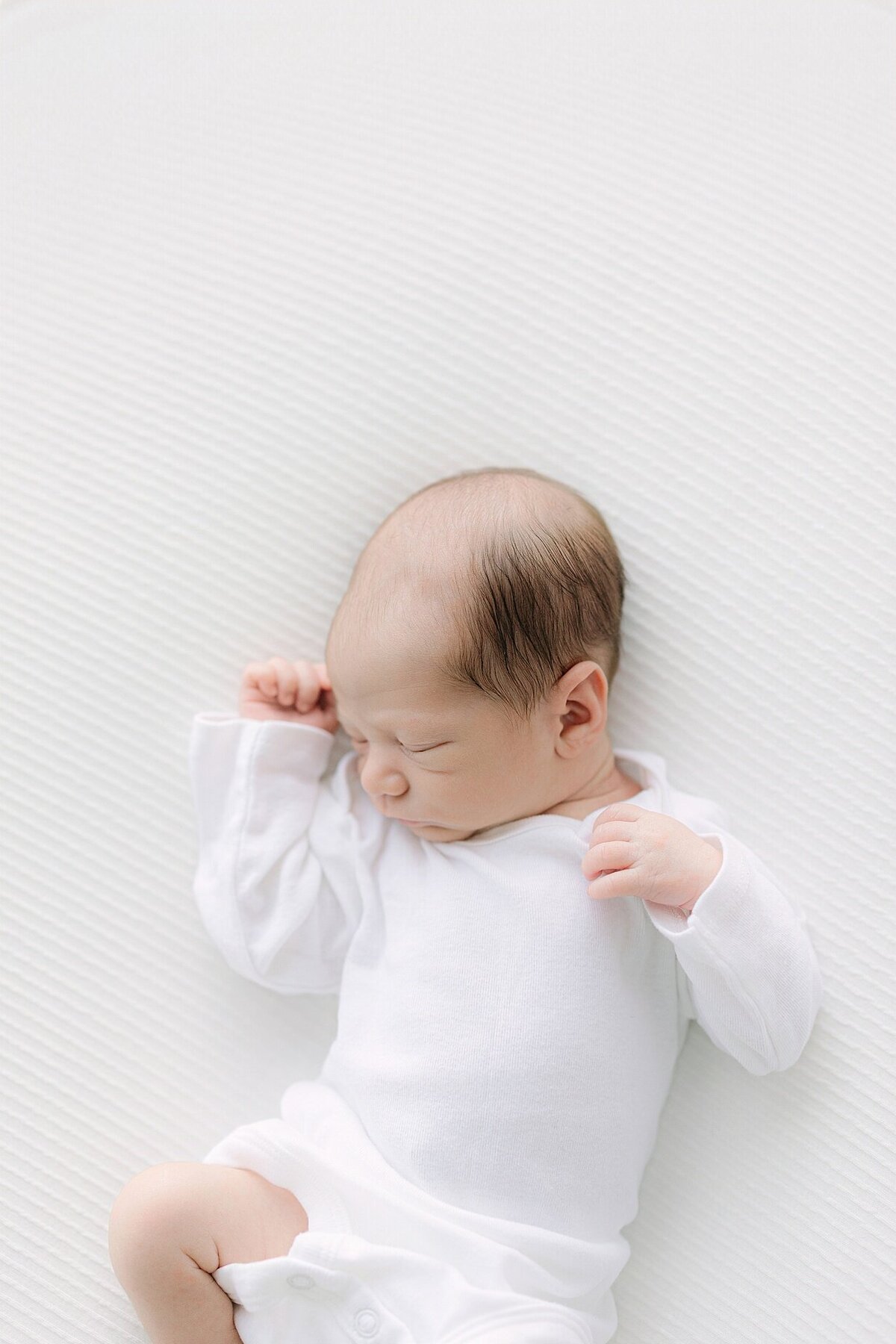 Newborn baby sleeping peacefully in a white onesie during a session with an Indianapolis newborn photographer