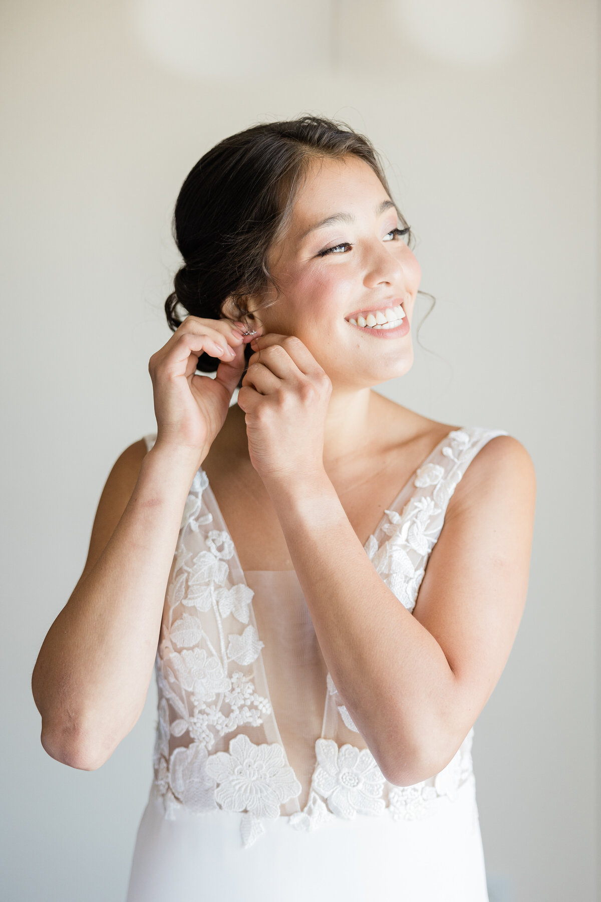 Bride in wedding dress smiling at light while putting on earing