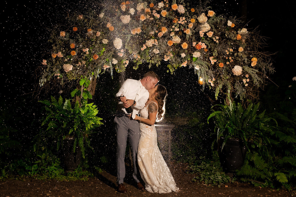 Bride and groom kiss spraying champagne at night at Camrose Hill Flower Farm in Stillwater, Minnesota.