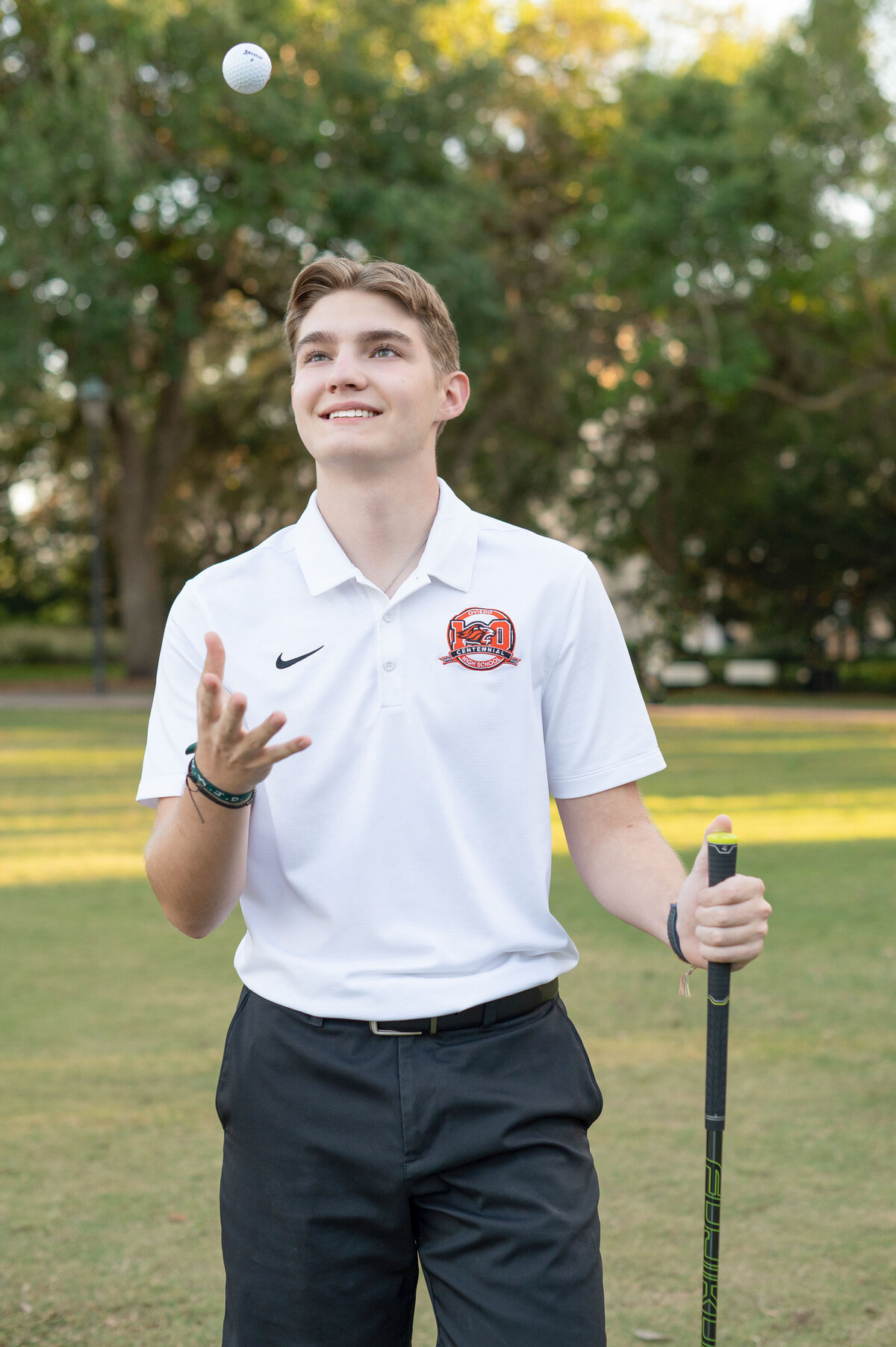 High school senior boy holding golf club throws golf ball into the air.